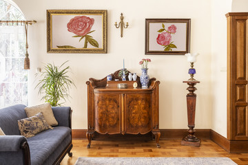 real photo of an antique cabinet with porcelain decorations, paintings with roses and blue sofa in a