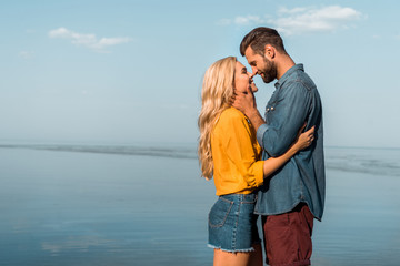 side view of smiling girlfriend and boyfriend touching with noses on beach