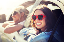 Summer Holidays, Valentines Day, Travel, Road Trip And People Concept - Happy Teenage Girls Or Young Women Heart Shaped Sunglasses In Car At Seaside
