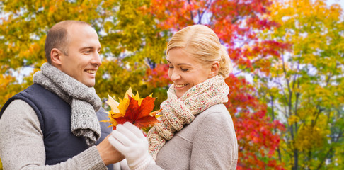 Poster - love, relationships and people concept - smiling couple with maple leaves over autumn park background