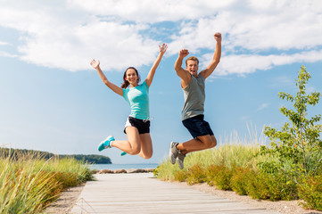 Poster - fitness, sport and lifestyle concept - happy couple in sports clothes jumping on beach