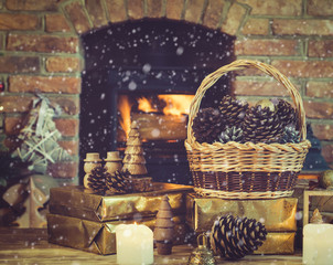 Wall Mural - Christmas composition, pine cones in wicker basket, wooden ornaments, golden presents on the table in front of fireplace with woodburner, candles and garlands, selective focus, snow, toned