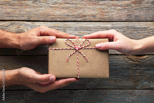 Fotografie, Obraz Female hands holding gift box with rope on wooden table