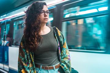 Young brunette woman with long curly hair using waiting for the subway metro in Madrid wearing glasses hipster stylish