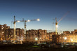building site with three tower cranes against the background of multi-storey houses and a blue sky, night scene