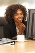 © Mark Adams - Millennial black businesswoman sitting at computer desk and smiling at camera