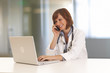 © Mark Adams - Portrait of young woman doctor in white coat at computer using phone