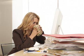 Young businesswoman drinking coffee at desk indoors office building