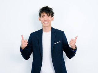 Portrait of handsome Chinese young man in dark blue leisure suit posing against white wall background. Make two  thumb up gesture and looks so happy.