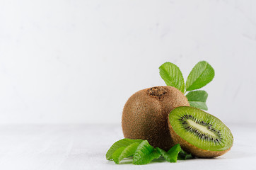 Exotic fruts  closeup - juicy ripe fleshy kiwi with slice, drop juice and young green leaves in elegant white kitchen interior.