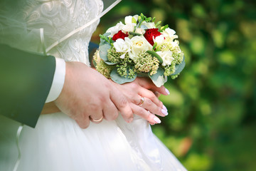 wedding rings on the fingers of the bride and groom on a bridal bouquet