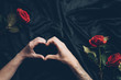 © LIGHTFIELD STUDIOS - cropped shot of couple showing hand heart symbol above black fabric with red roses