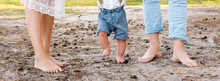 Happy Family In The Forest. Closeup Of Feet Of Family With Little Baby Boy Walking Barefoot On Sand. Man And Woman Holding Their Toddler Child.