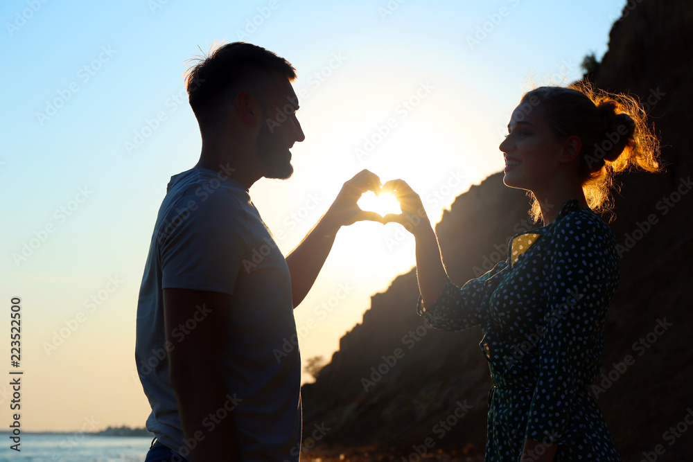 Cute young couple making heart with their hands on sea shore