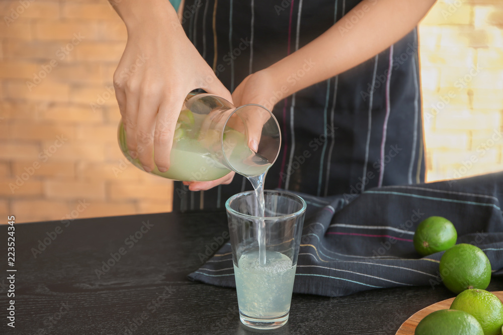 Woman pouring fresh lime lemonade from jug into glass