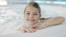 Pretty Little Girl With Wet Hair Is Sitting Alone In Hydromassage Bath In A Water Park, Looking To Camera
