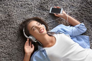 Canvas Print - Beautiful young woman listening to music while lying on carpet at home