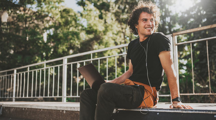 Poster - Handsome male with curly hair using laptop computer chatting online with friends using earphones and laptop connected to free wireless. Cheerful male blogger publishing post on website on computer.