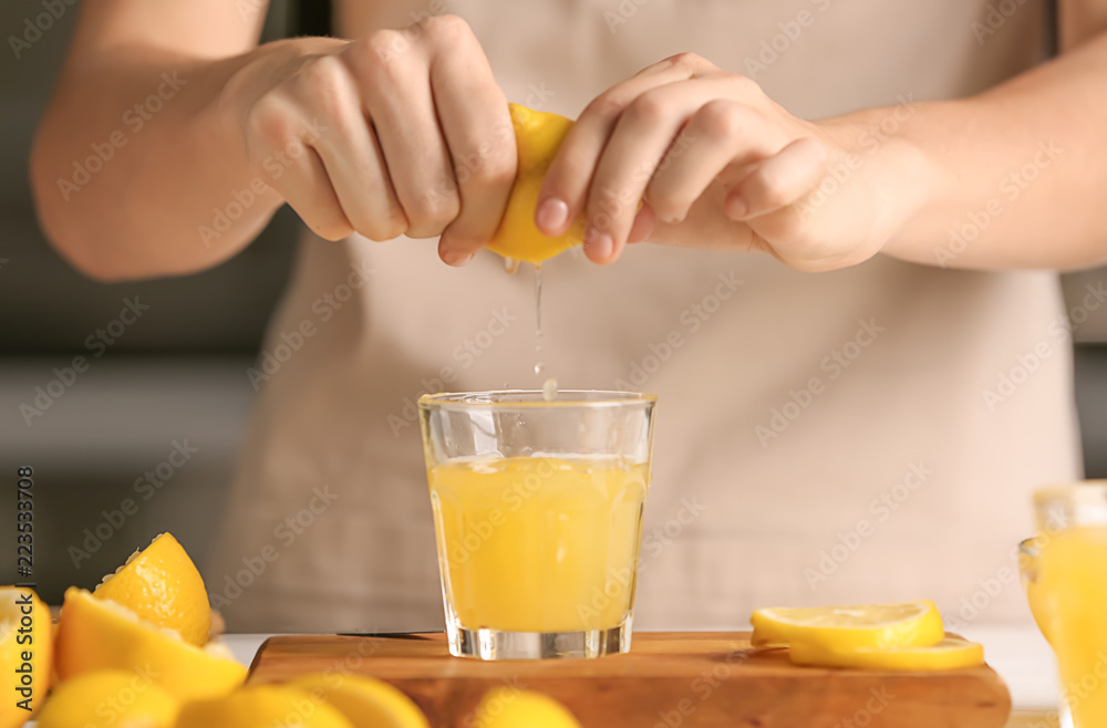 Woman squeezing fresh lemon juice into glass at table