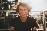Fototapeta  - Outdoor closeup portrait of handsome freckled smiling male with curly hair, posing for social advertisement, in the city street on sunset sunlight with copy space for your promotional information