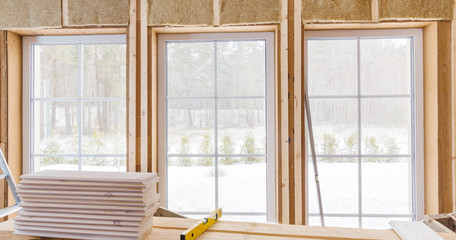 Thermally insulating eco-wood frame house with wood fiber plates and heat-isolating natural hemp material. Finishing the walls and a large window with a white wooden board, using laser line level.