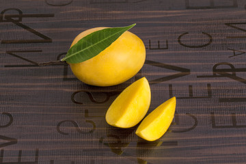 Wall Mural - A Mango with leaf and stem and some cut slices of mango on brown background