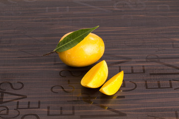 Wall Mural - A Mango with leaf and stem and some cut slices of mango on brown background