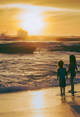 Children watching the sunset as waves and surf roll in at the beach