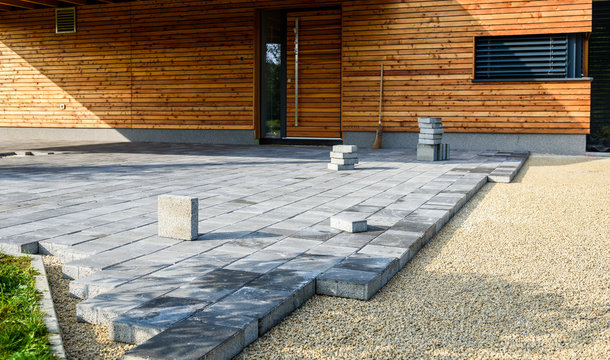 laying gray concrete paving slabs in house courtyard driveway patio.