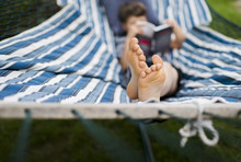 High Angle View Of Boy Reading Book While Relaxing On Hammock At Yard