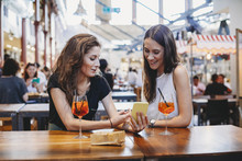 Woman Showing Mobile Phone To Female Friend At Table In Restaurant