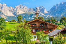Typical Wooden Alpine House Against Alps Mountains Background On Green Meadow In Going Am Wilden Kaiser Village On Sunny Summer Day, Tyrol, Austria