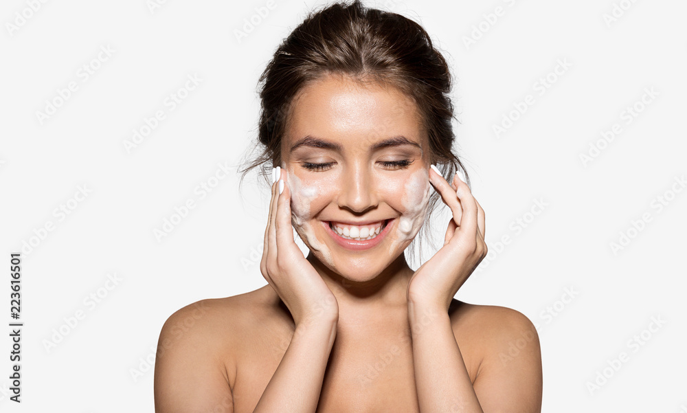 Portrait of cheerful laughing woman applying foam for washing on her face. Lovely brunette with attractive appearance. Skincare spa relax concept. Isolated on grey background - obrazy, fototapety, plakaty 