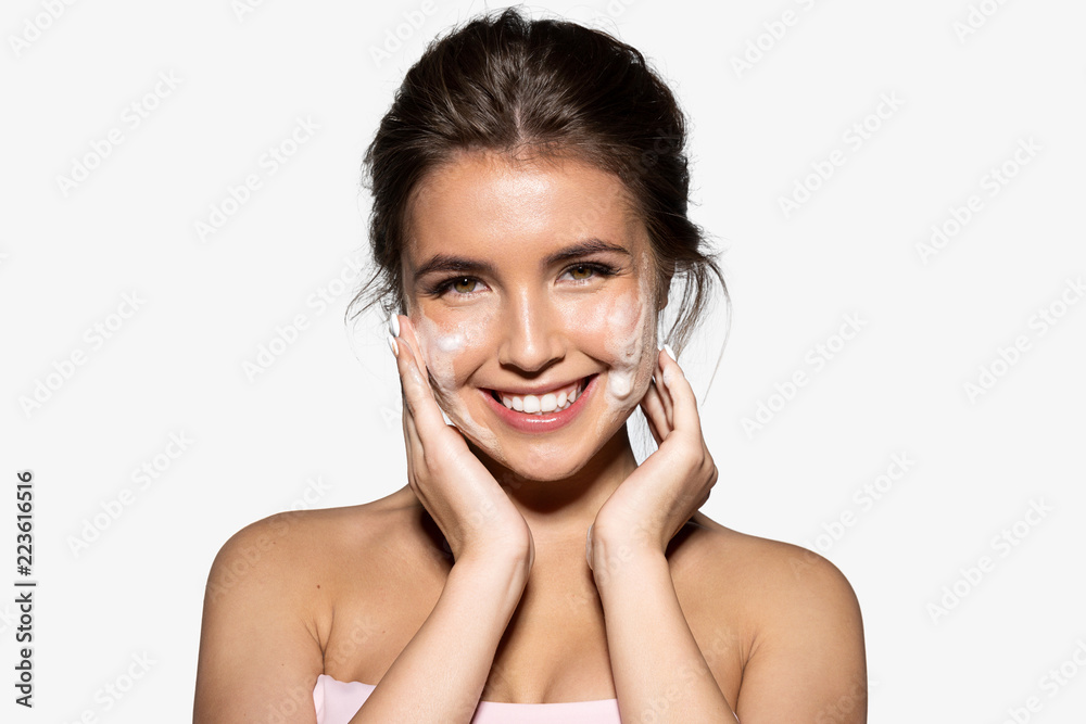 Portrait of joyful young woman applying white foam for washing. Cheerful brunette with perfect clean skin looking at camera with gladness. Skincare spa relax concept. Isolated on grey background - obrazy, fototapety, plakaty 