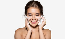 Portrait Of Cheerful Laughing Woman Applying Foam For Washing On Her Face. Lovely Brunette With Attractive Appearance. Skincare Spa Relax Concept. Isolated On Grey Background