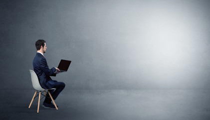 Canvas Print - Businessman staying in an empty grey dark room with stuffs on his lap
