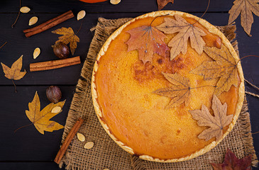 American homemade pumpkin pie with cinnamon and nutmeg, pumpkin seeds and autumn leaves on a wooden table. Thanksgiving food. Top view. Flat lay