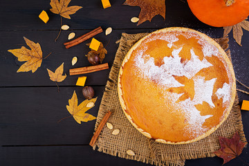 American homemade pumpkin pie with cinnamon and nutmeg, pumpkin seeds and autumn leaves on a wooden table. Thanksgiving food. Top view. Flat lay