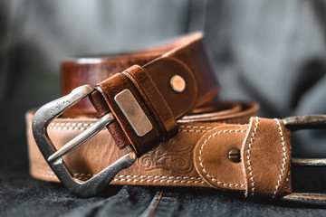 two brown leather belts on dark background