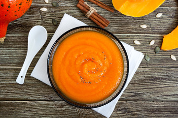 Wall Mural - Delicate pumpkin puree in a black glass bowl on a wooden table. Top view.