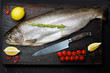 Fresh whole salmon with seasonings and a knife lies on a wooden dark background.
