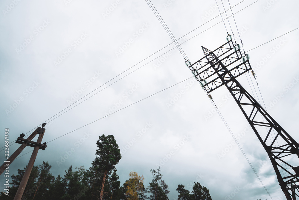 High voltage power lines among trees under cloudy sky. Electricity ...