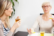 © Ivan - Senior mother and daughter talking and drinking tea in brightly lit dining room. Happy family moments at home