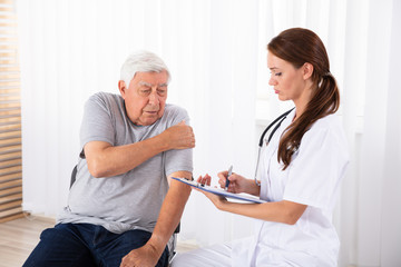 Doctor Giving Prescription To Male Patient Having Arm Pain