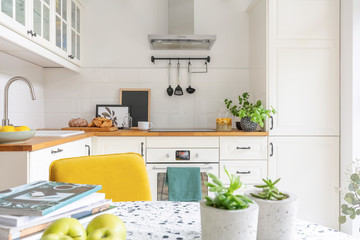 Close-up of a table with fruit, plants and magazines in a bright kitchen interior. Cupboards in the background. Real photo