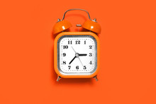 Vintage Style Orange Metal Alarm Clock With Bells Standing On The Orange Surface Isolated. Back To School Concept. Free Space For Text