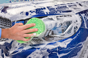 Wall Mural - Man washing a soapy blue car with a green sponge.