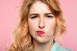 facial expression. quizzical grumpy thoughtful woman. young beautiful blond girl portrait on pink background.