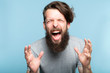 © golubovy - emotional breakdown. angry enraged infuriated crazy man screaming. portrait of a young bearded guy on blue background. emotion facial expression. feelings and people reaction.