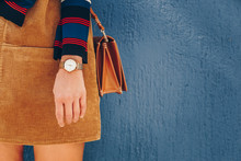 Close Up, Young Fashion Blogger Wearing A Corduroy Dress And A White And Golden Analog Wrist Watch. Checking The Time, Holding A Beautiful  Leather Purse. Street Style Fashion Details. 